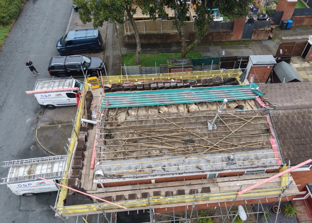 Drone view of a roof stripped back to the timbers, with two D & P vans on the street below